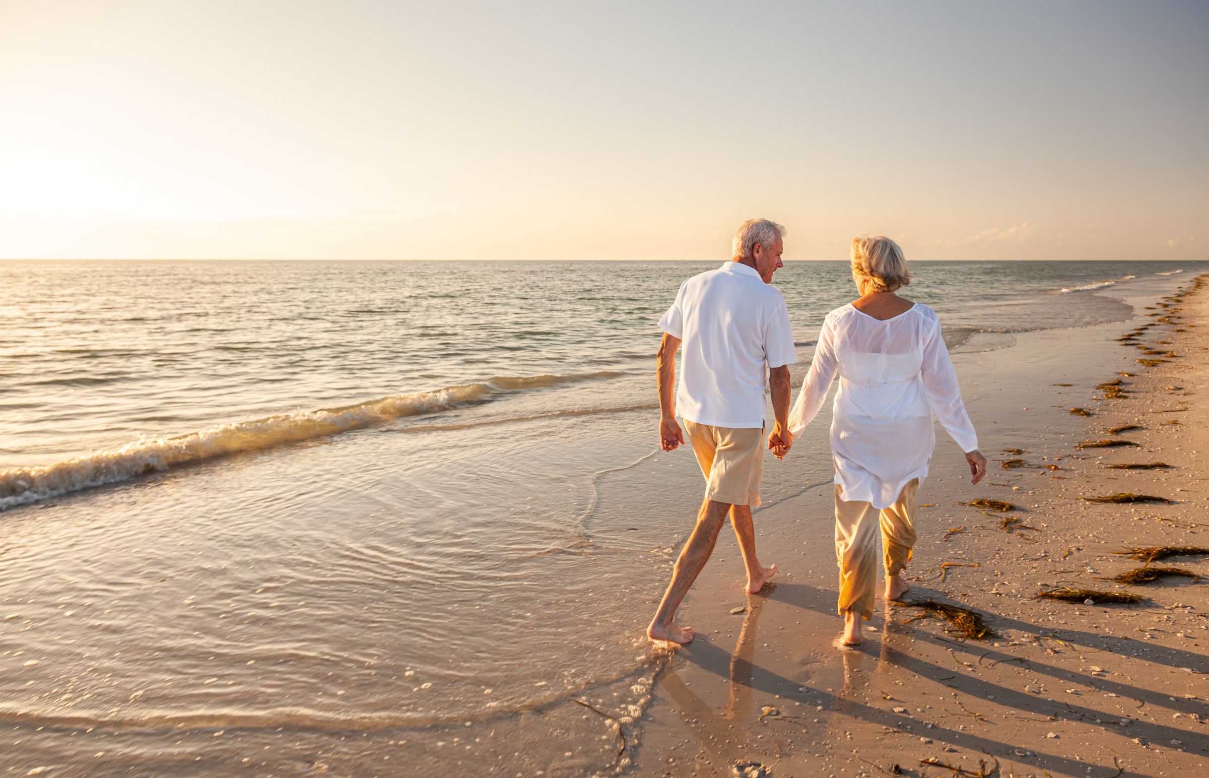 An older couple walking hand in hand along the shoreline at sunset